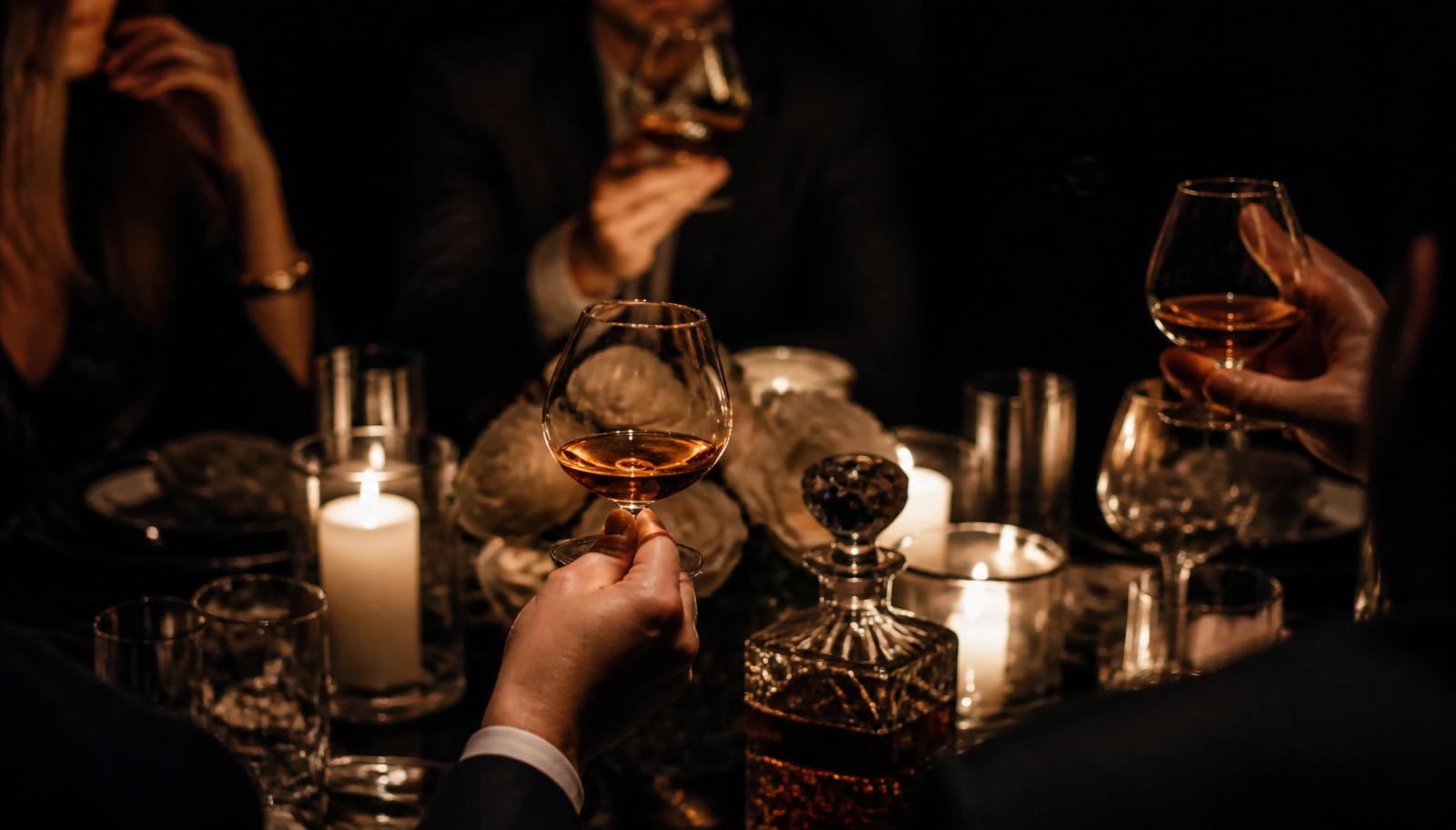 Guests holding cognac glasses at a candlelit table